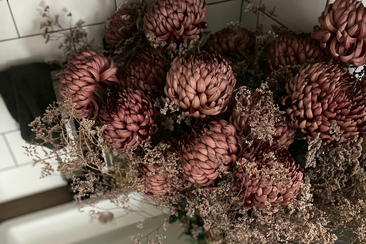 Big bouquet of dusty plum chrysanthemums with dried pink filler flowers, seen from above over a white sink