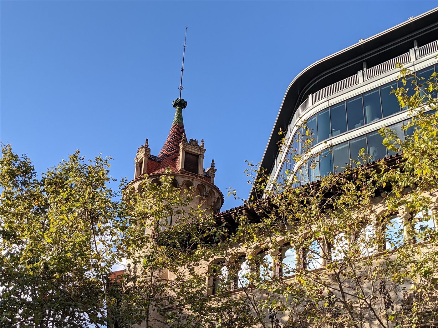 A Modernista tower beside a curved glass building in Barcelona, old and new side by side