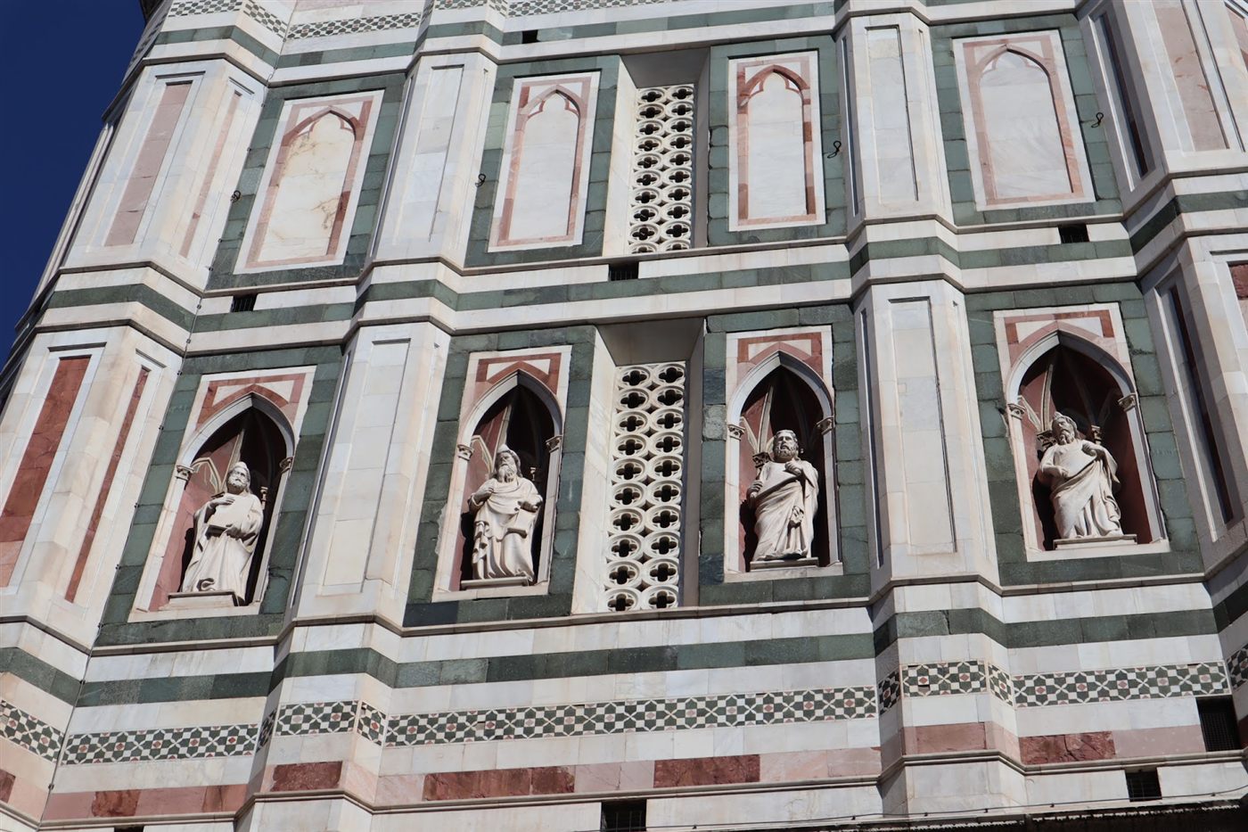 Green, white and pink marble panels and statues in niches on a bell tower in Florence