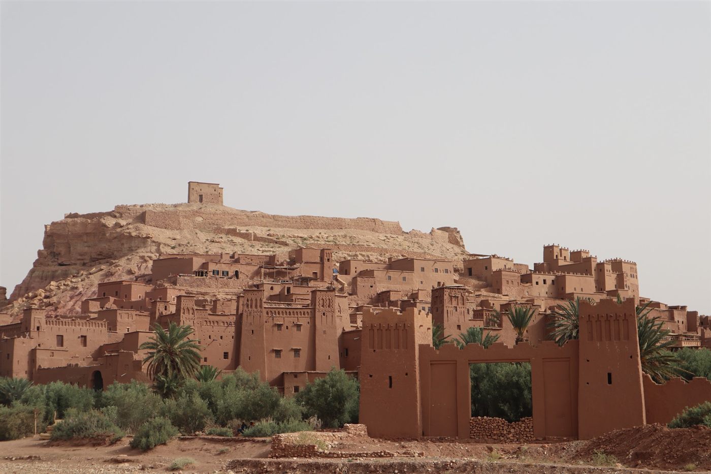 The mud-brick ksar of Ait Ben Haddou rising up a hill behind palm trees