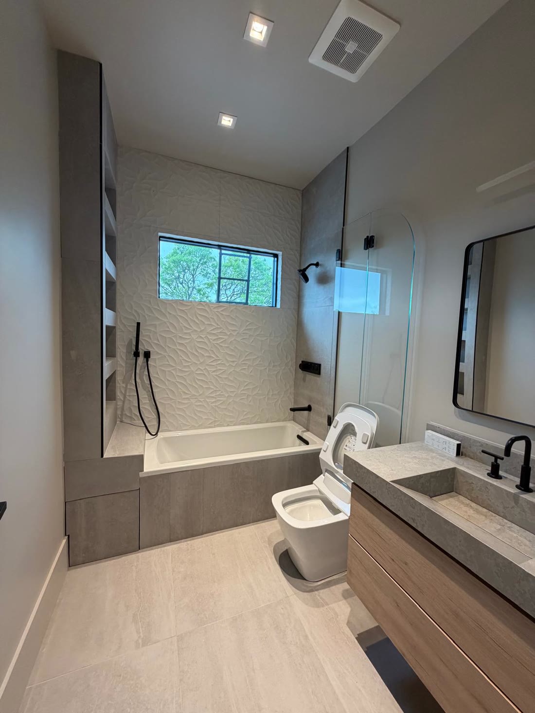 A family bathroom with a textured tile bath surround and a stone topped oak vanity