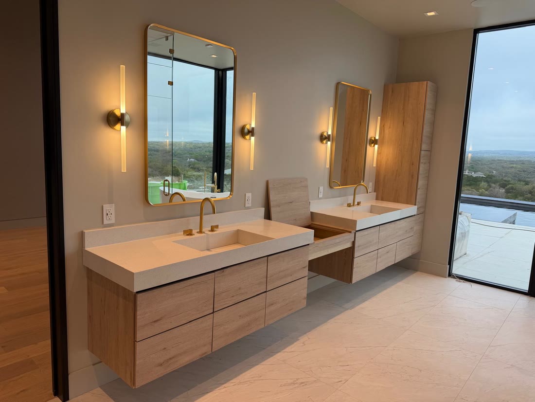 The principal vanity run in pale oak with brass sconces and mirrors, glazing to the hills beyond