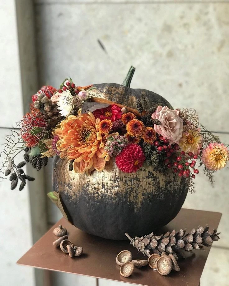 Black and gold brushed pumpkin overflowing with orange dahlias, roses and berries