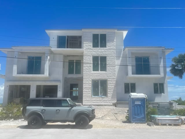 The house under construction: three storeys in white stucco with the ledgestone spine up the centre, windows in, scaffolding gone